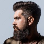 Side view portrait of stylish young man. Perfect beard. Close-up of young bearded man, stylish hairstyle, beard. Side view bearded man isolated on gray background. Man's haircut in barber shop
