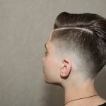 Stylish modern retro haircut side part with mid fade with parting of a school boy guy in a barbershop on a brown background